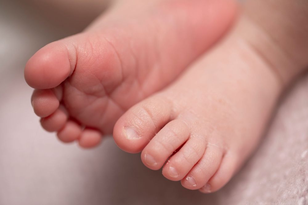 Close-up of tiny newborn baby feet with soft pink skin resting on a light blanket.