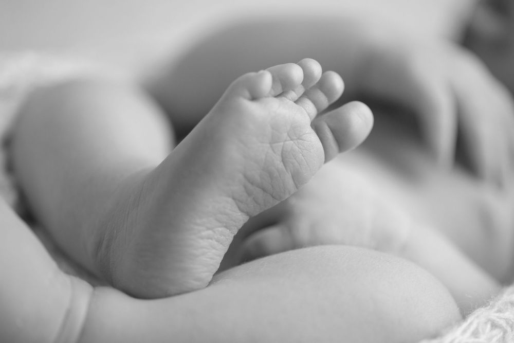 Close-up black and white photo of a newborn baby's tiny feet, showcasing delicate skin and small toes.
