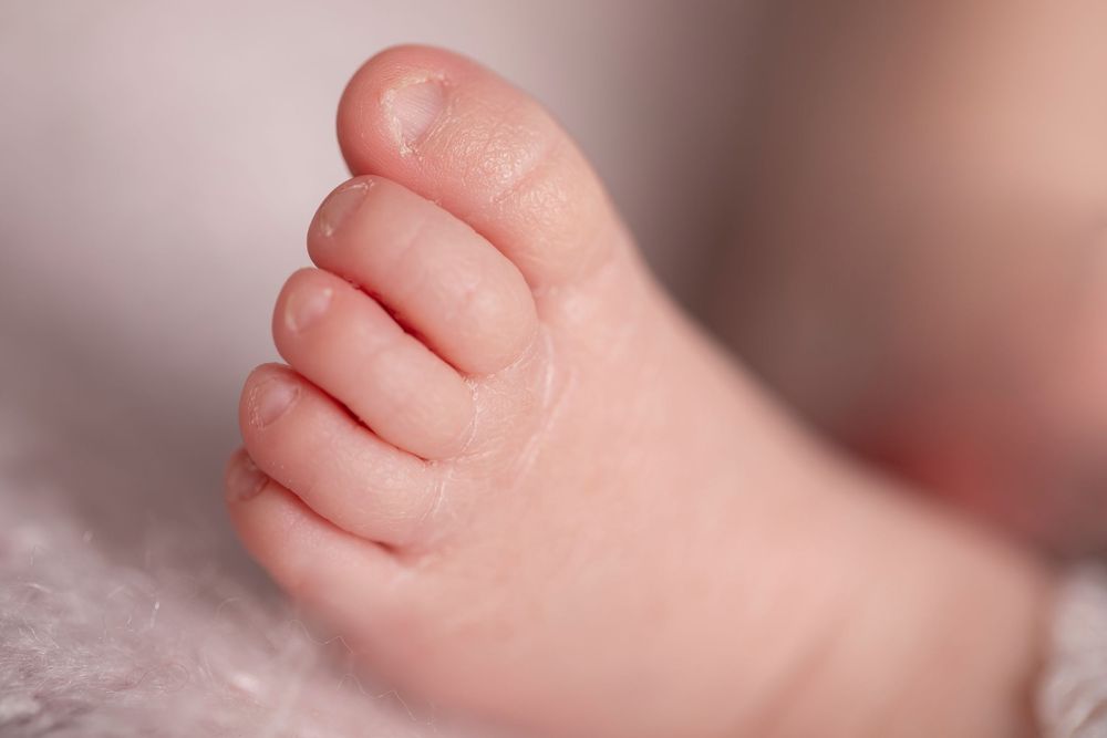 Close-up of a newborn baby's tiny foot with delicate toes resting on a soft white blanket.