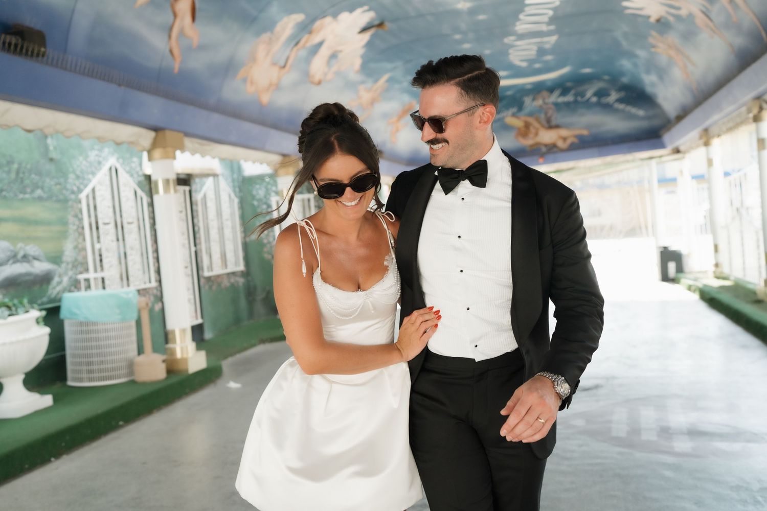 Black and white photo of a bride and groom walking outdoors, her long lace veil billowing in the wind.