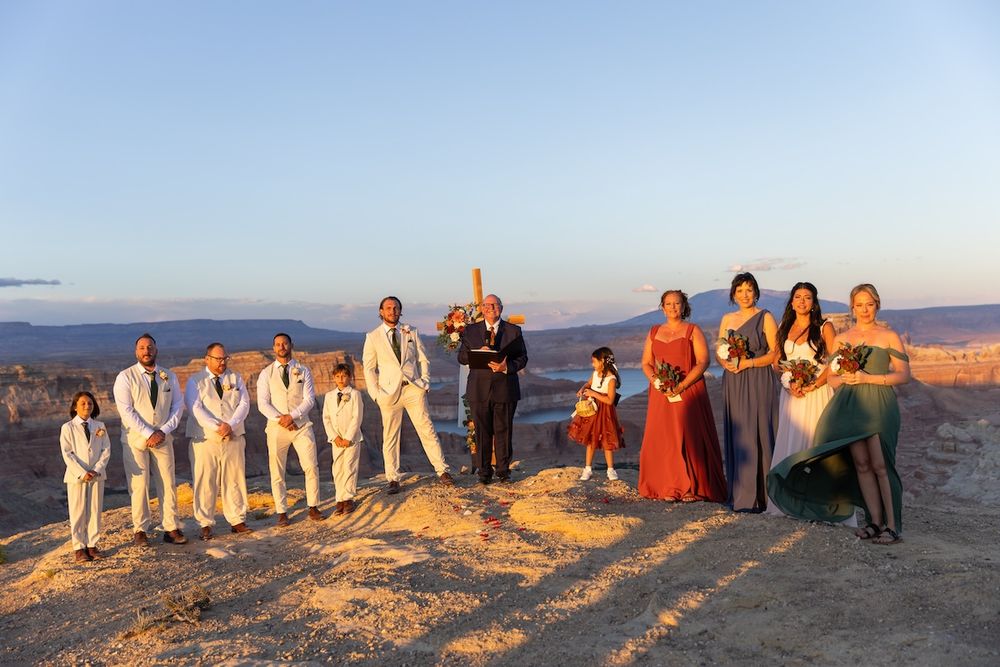 A wedding party poses together on a rocky overlook at sunset with a scenic canyon landscape in the background.