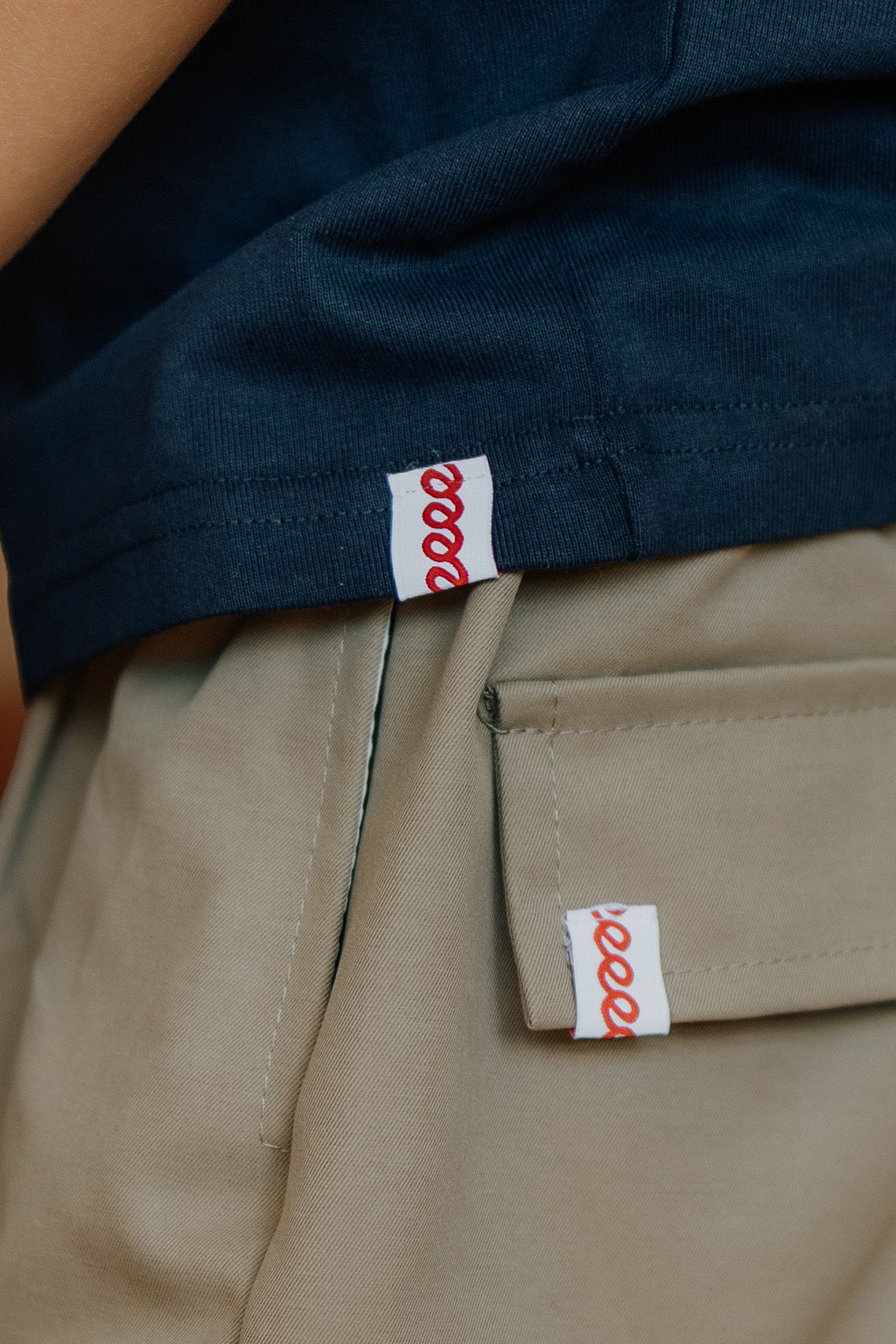 Close-up of navy t-shirt and khaki pants with matching red script logo tags on both garments.