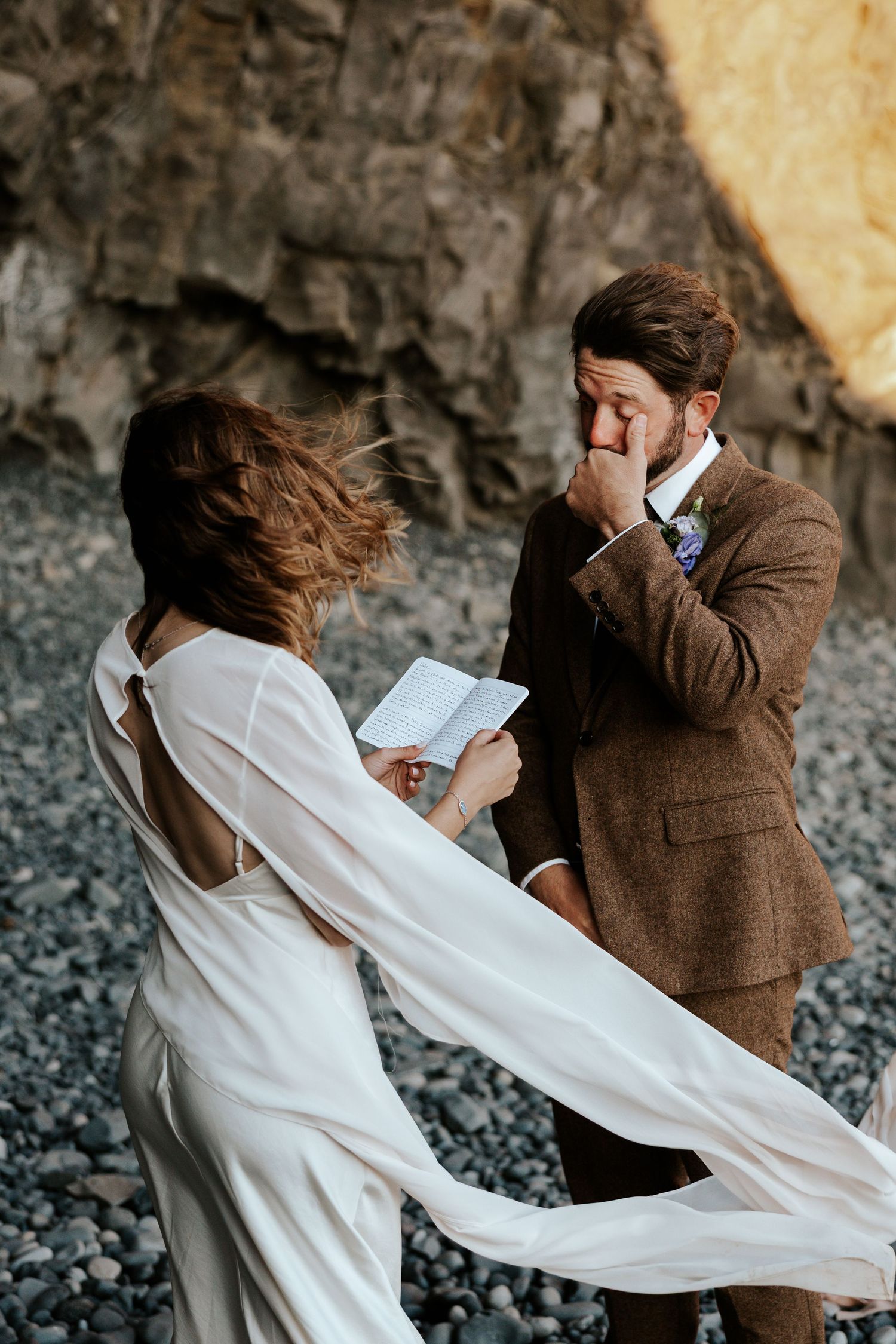 candid moment of bride reading vows to groom while groom wipes a tear from his eye at Reynisfjara Beach in iceland