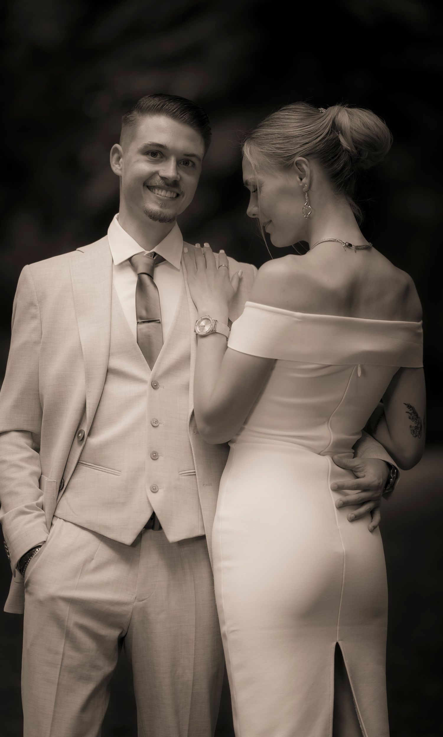 Bride and groom posing elegantly in sepia-toned wedding portrait outdoors.