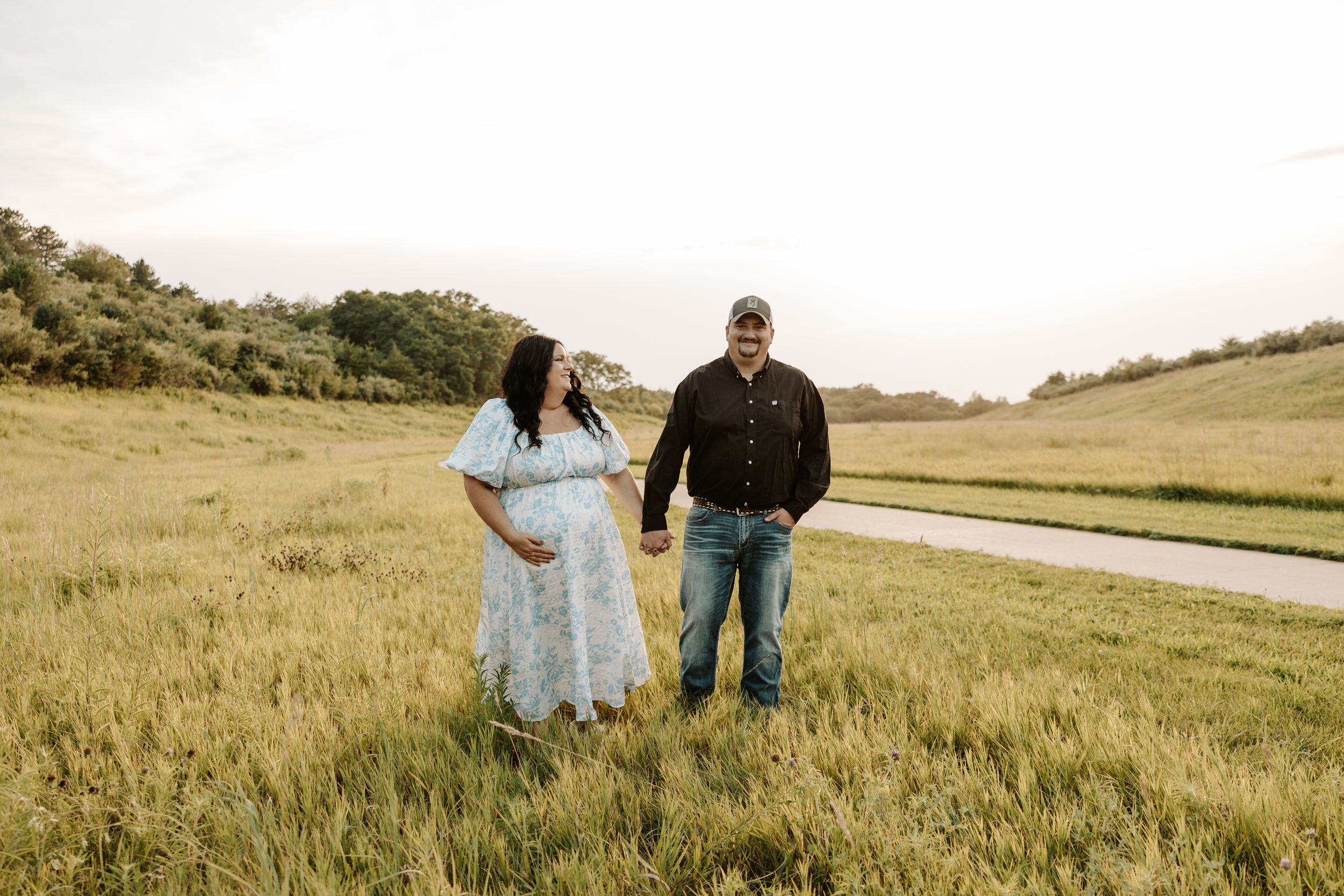 Pregnant couple holding hands in a lush green field during a maternity photo session outdoors.