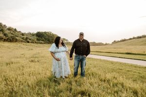 Pregnant couple holding hands in a lush green field during a maternity photo session outdoors.