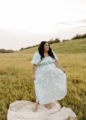 Woman in floral blue maxi dress twirling in golden meadow field at sunset.