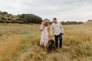 Couple walking with their dog in a golden meadow field during an outdoor engagement photo session.