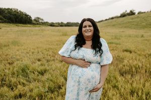 Pregnant woman in floral blue dress smiling in a green field during a maternity photo shoot.