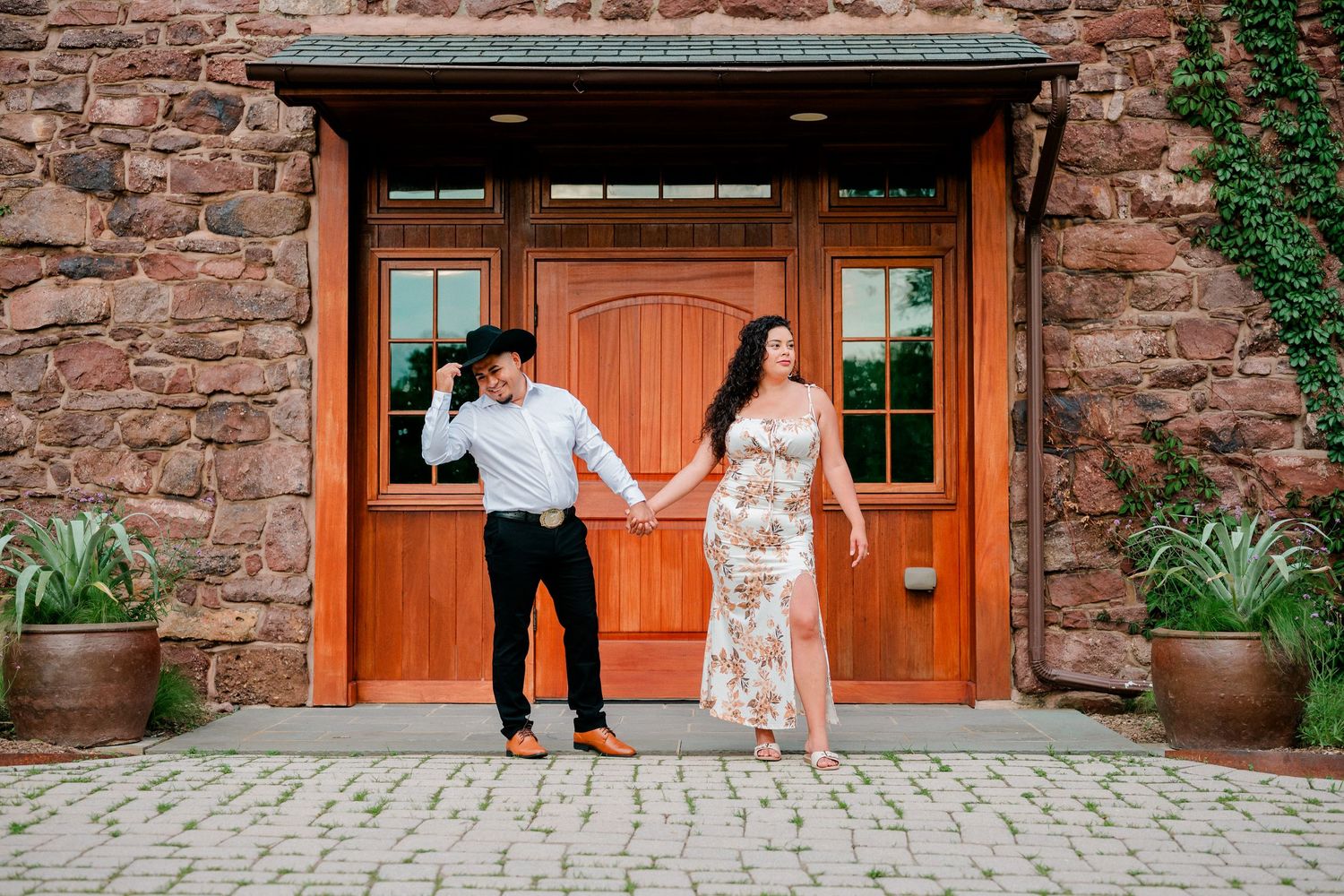 Denise and Santiago holding hands in front of historic stone doors during their Willowwood Arboretum engagement session in Far Hills NJ.