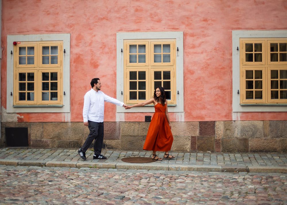 Couple holding hands dancing on cobblestone street beside pink building with windows.