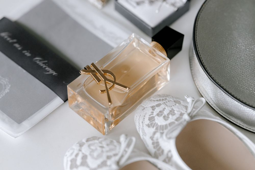 YSL Libre eau de parfum bottle with gold logo displayed alongside white lace heels and accessories on white surface.