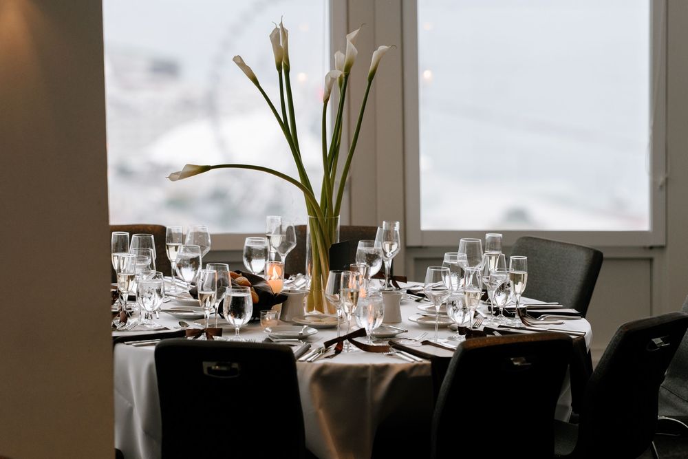 Elegant dining table set with crystal glasses and white calla lily centerpiece near a bright window.