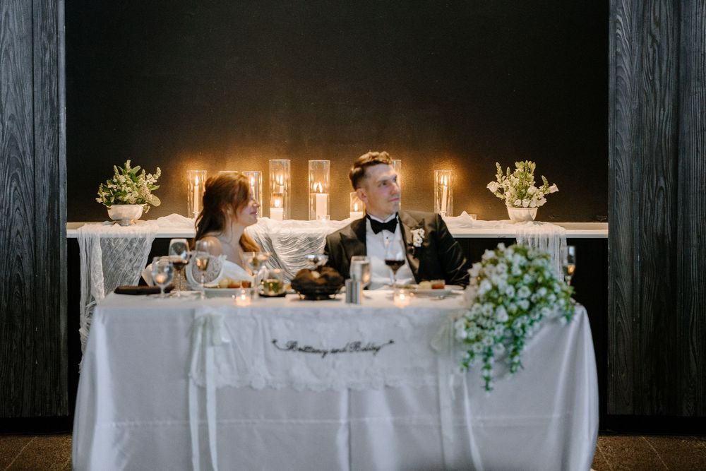 Bride and groom share intimate moment at elegant candlelit sweetheart table with white floral decor.