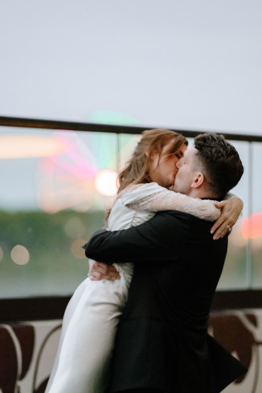 Bride and groom share a romantic kiss on a balcony with colorful bokeh lights in the background.