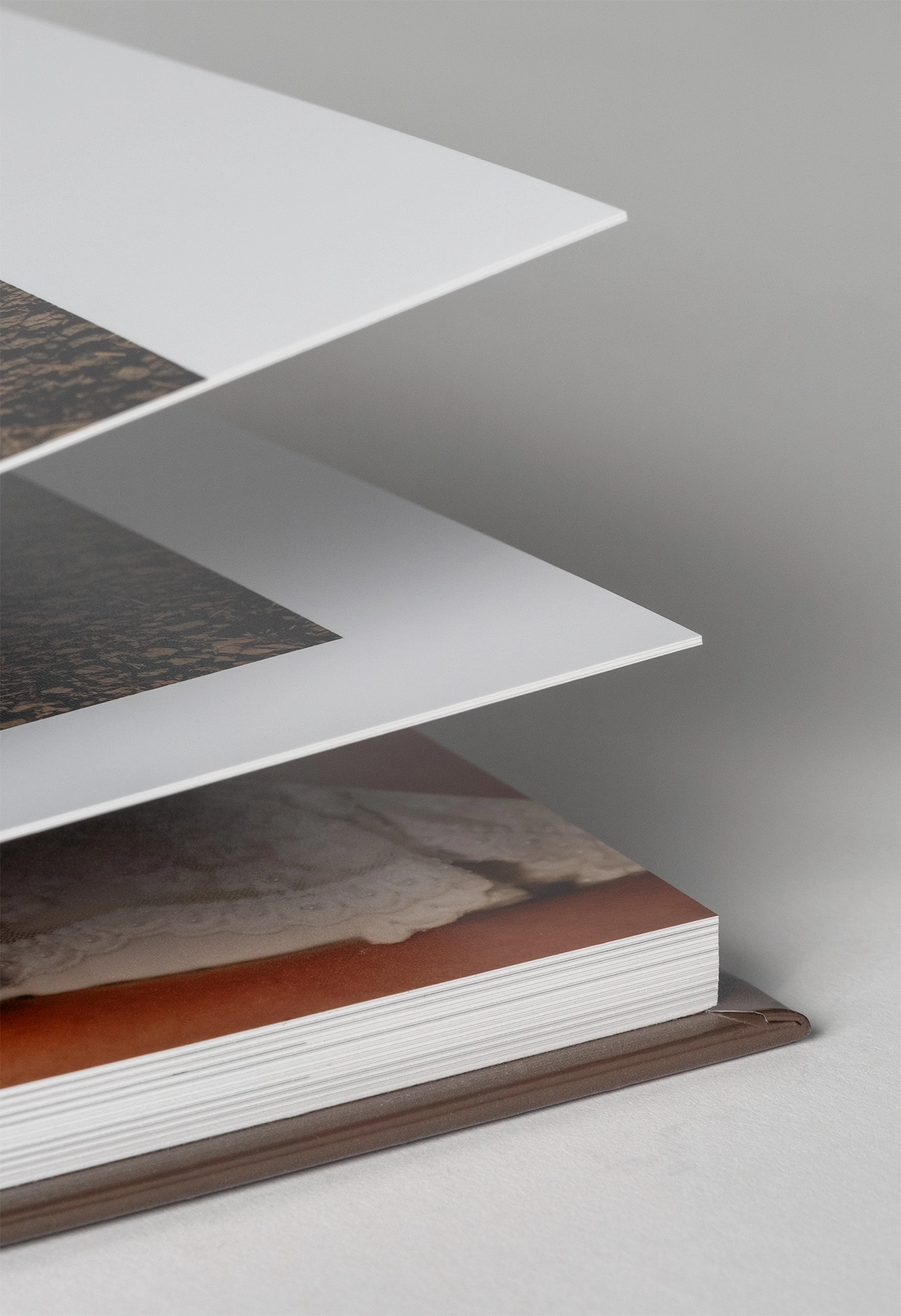 Layered pages of a photo book fanned out to show white paper edges against a gray background.