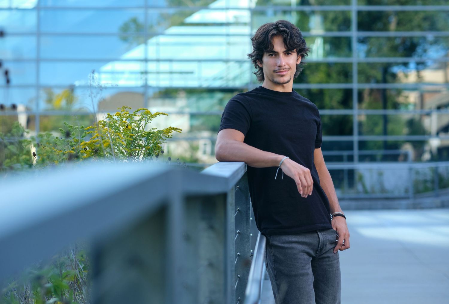 A young man leans on a railing for a senior photo in an Appleton Park.