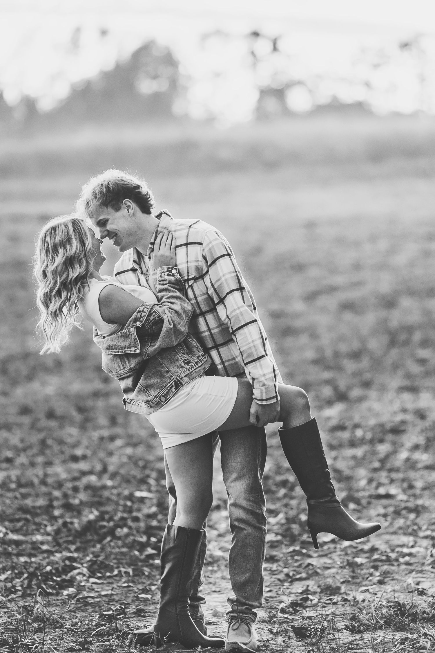 Black and white photo of a couple embracing in an open field, woman in mini skirt and boots, man in plaid shirt.