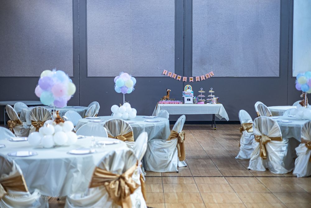 Elegant baby shower venue with white and gold chair covers, floral centerpieces, and a decorated dessert table.
