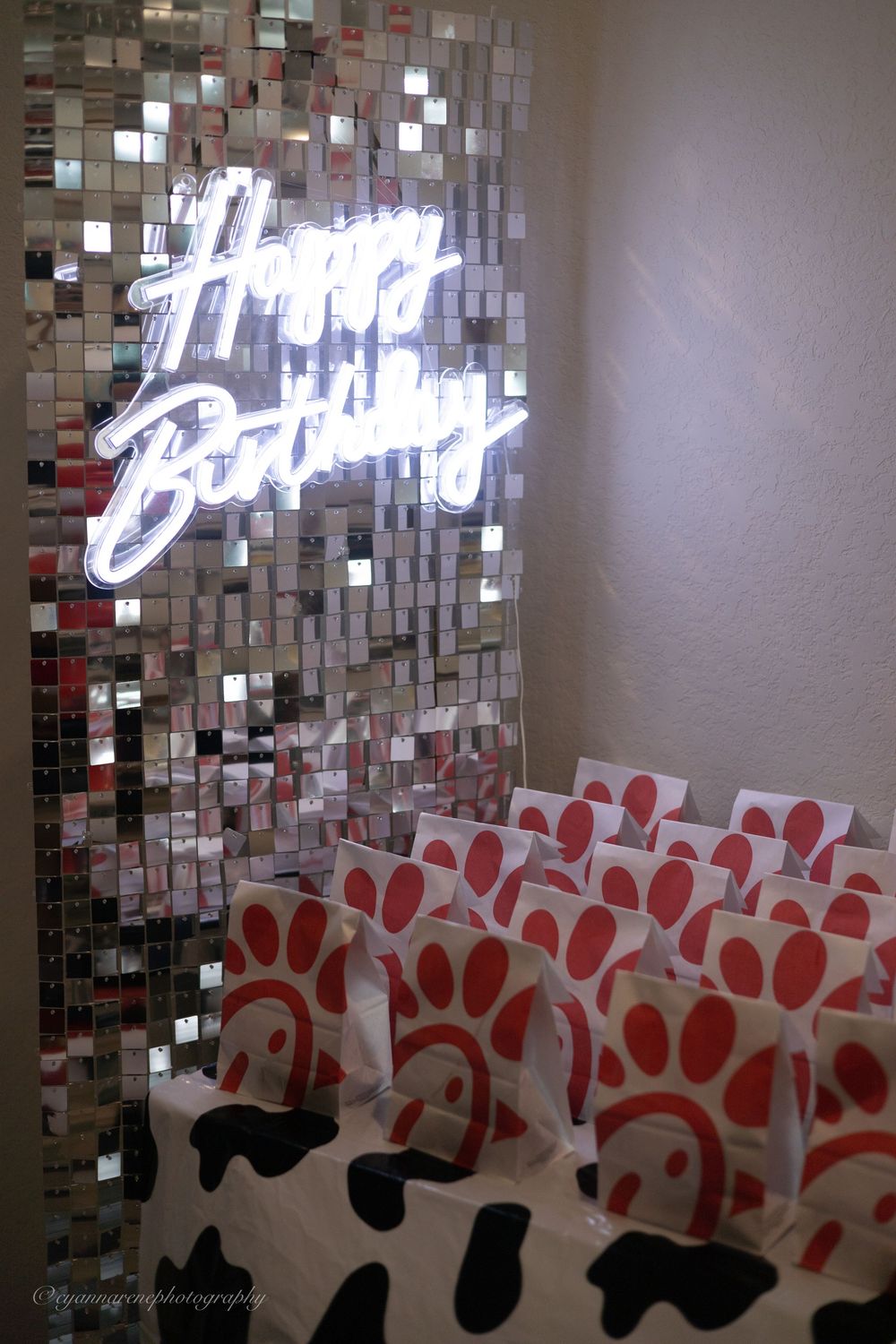 Happy Birthday neon sign on mirrored tile wall with Chick-fil-A gift bags arranged below for a birthday party.
