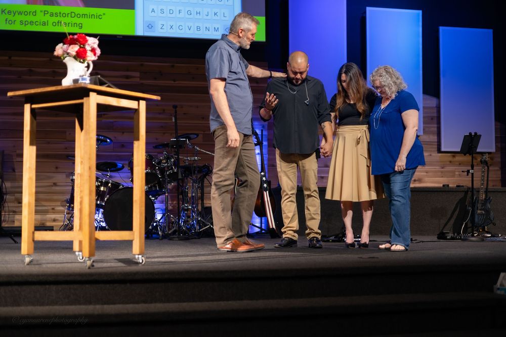 Four people praying together on a church stage near a wooden podium during a worship service.