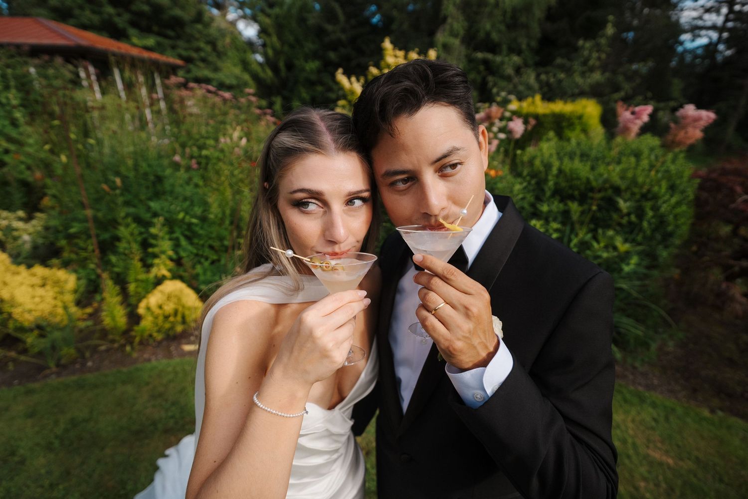 Madison and Ruben at their Froggsong Garden wedding sharing their signature cocktails together amongst lush bushes.