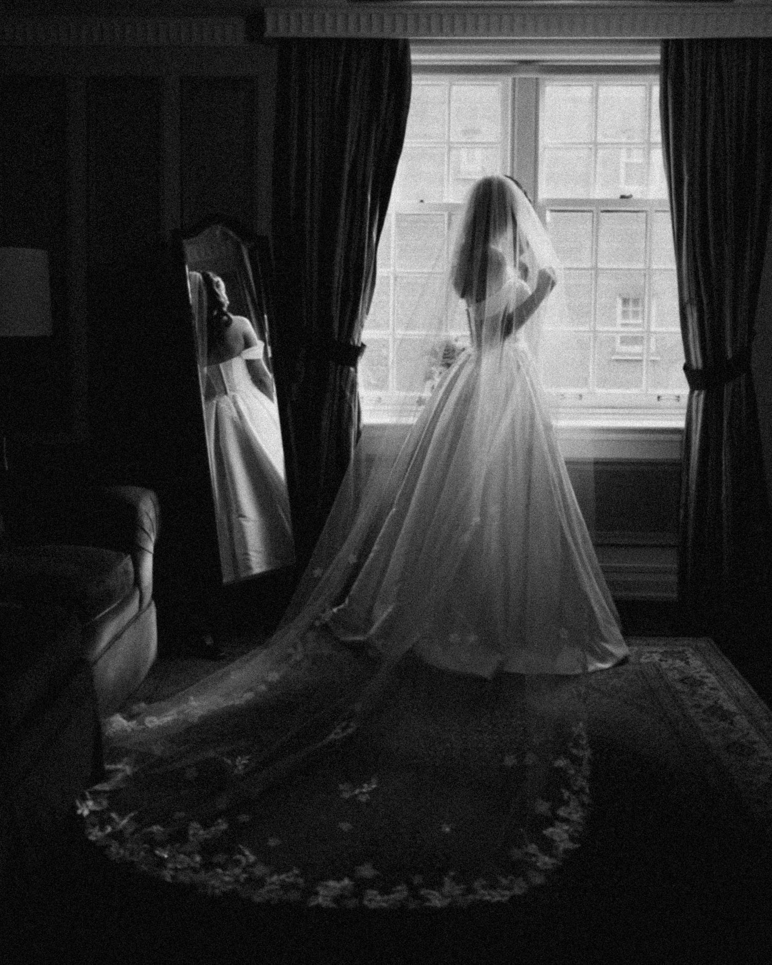Black and white wedding photo of bride showing engagement ring, wearing pearl necklace and white gown.