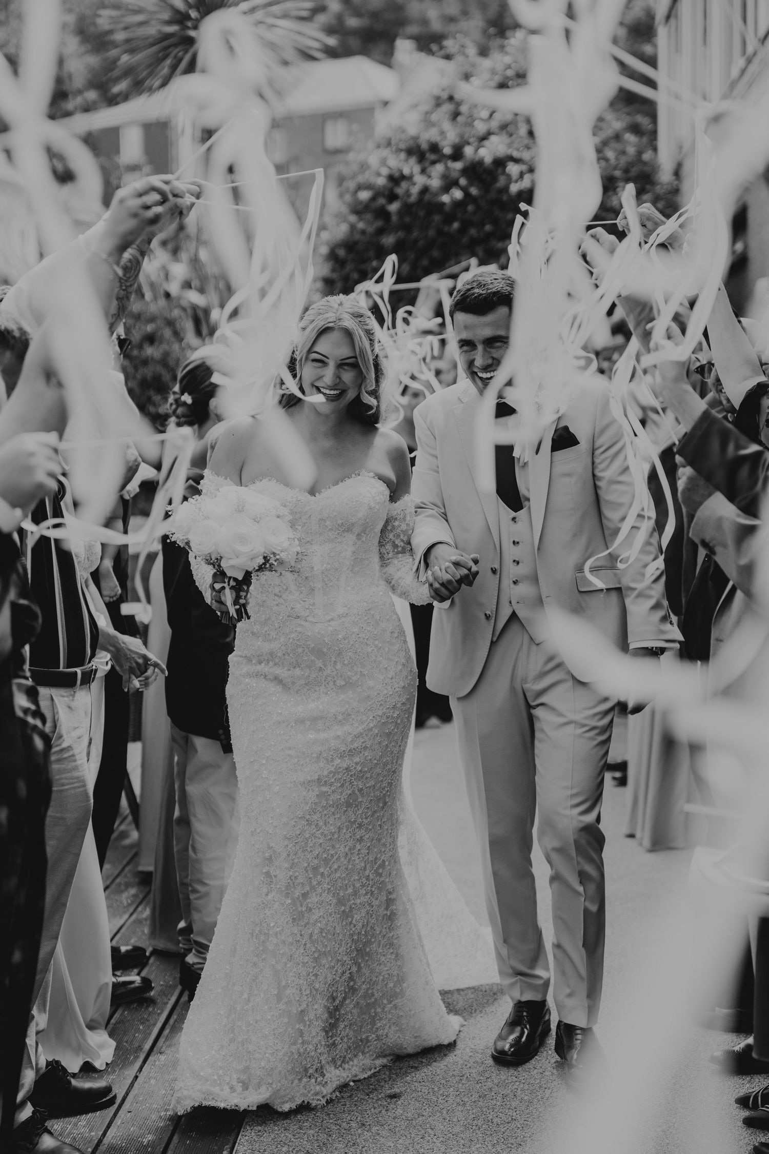 Black and white photo of a joyful bride and groom walking through a sparkler exit surrounded by cheering wedding guests.
