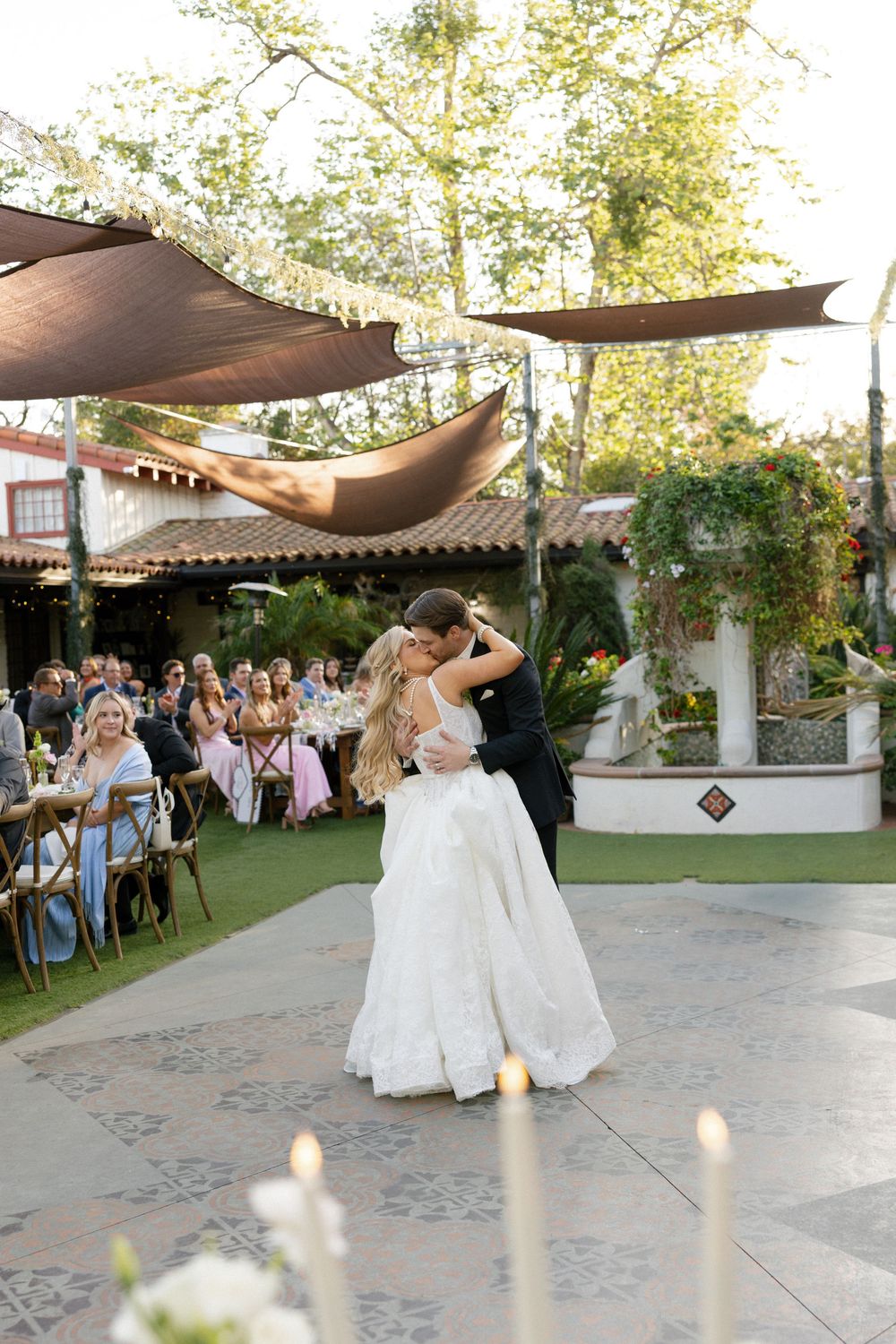 Bride and groom share first dance on outdoor patio at elegant garden wedding reception with candles.