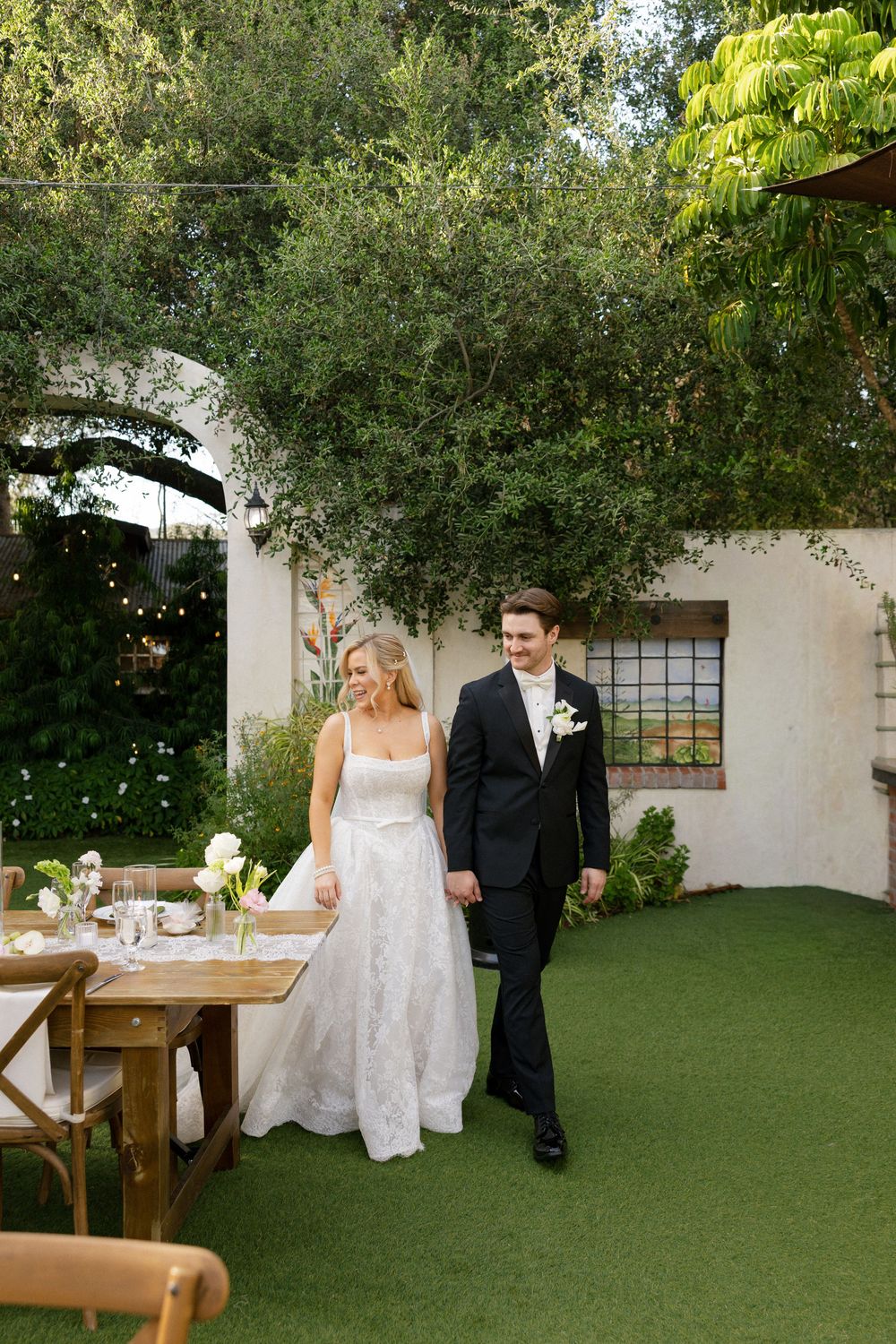 Bride and groom walking hand in hand through outdoor garden wedding reception venue.