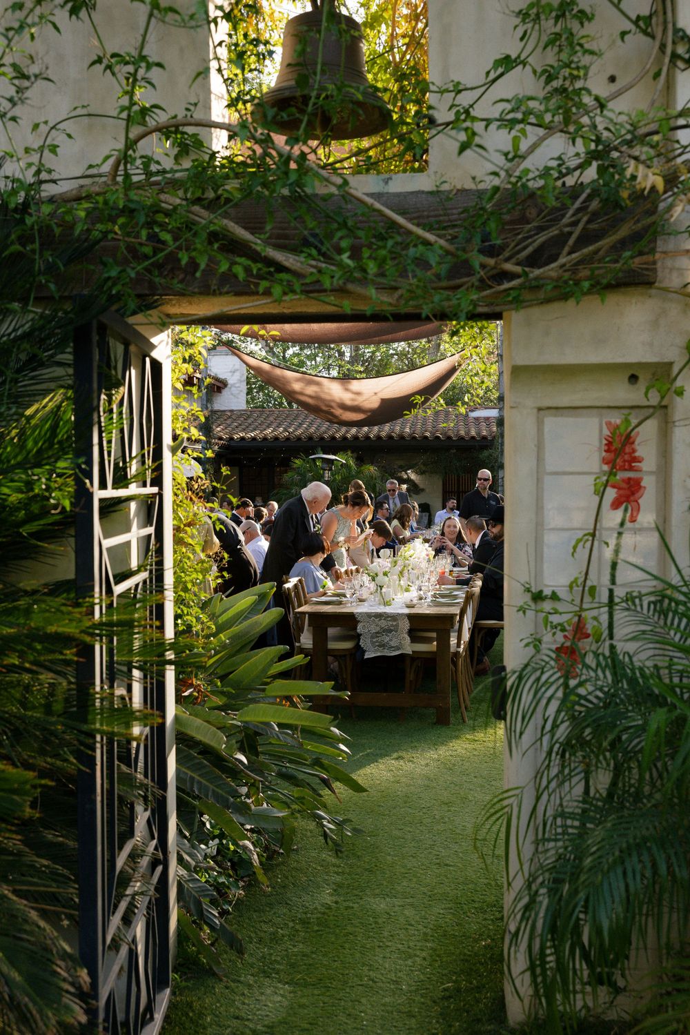 Elegant outdoor garden wedding reception viewed through lush tropical archway with long dining table.
