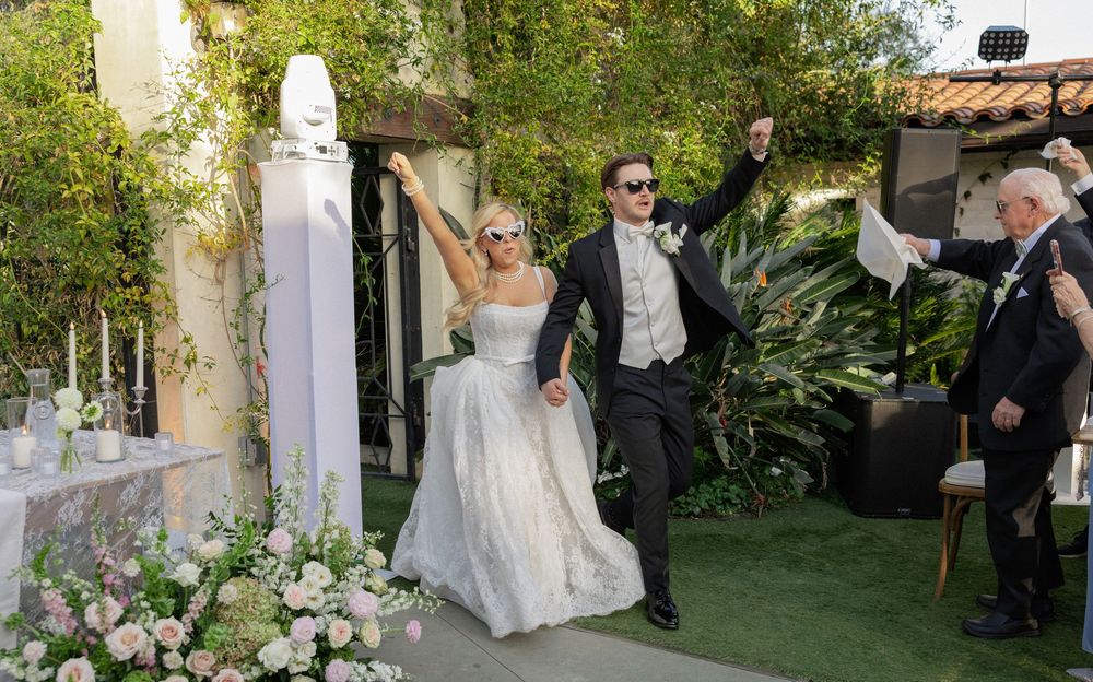 Bride and groom celebrate joyfully at outdoor garden wedding ceremony with floral arrangements.