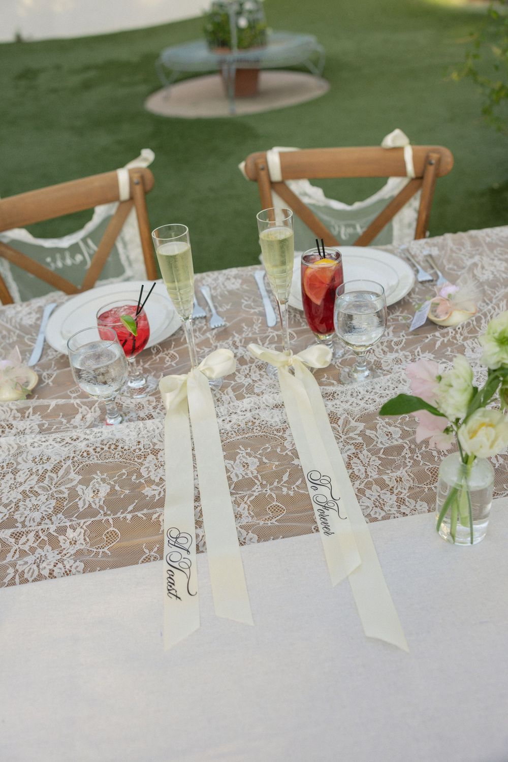 Elegant wedding sweetheart table with lace runner, floral arrangements, and bride groom ribbon signs.