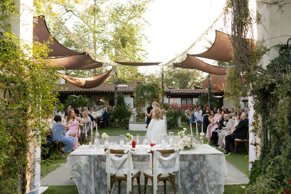Elegant outdoor wedding ceremony with canopy shading guests seated around decorated tables.