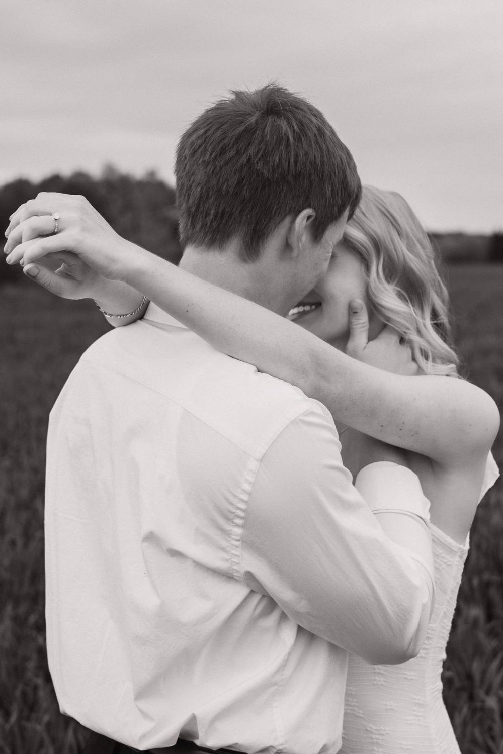 Black and white photo of a couple embracing romantically in a green field during their engagement shoot, North Carolina photographer