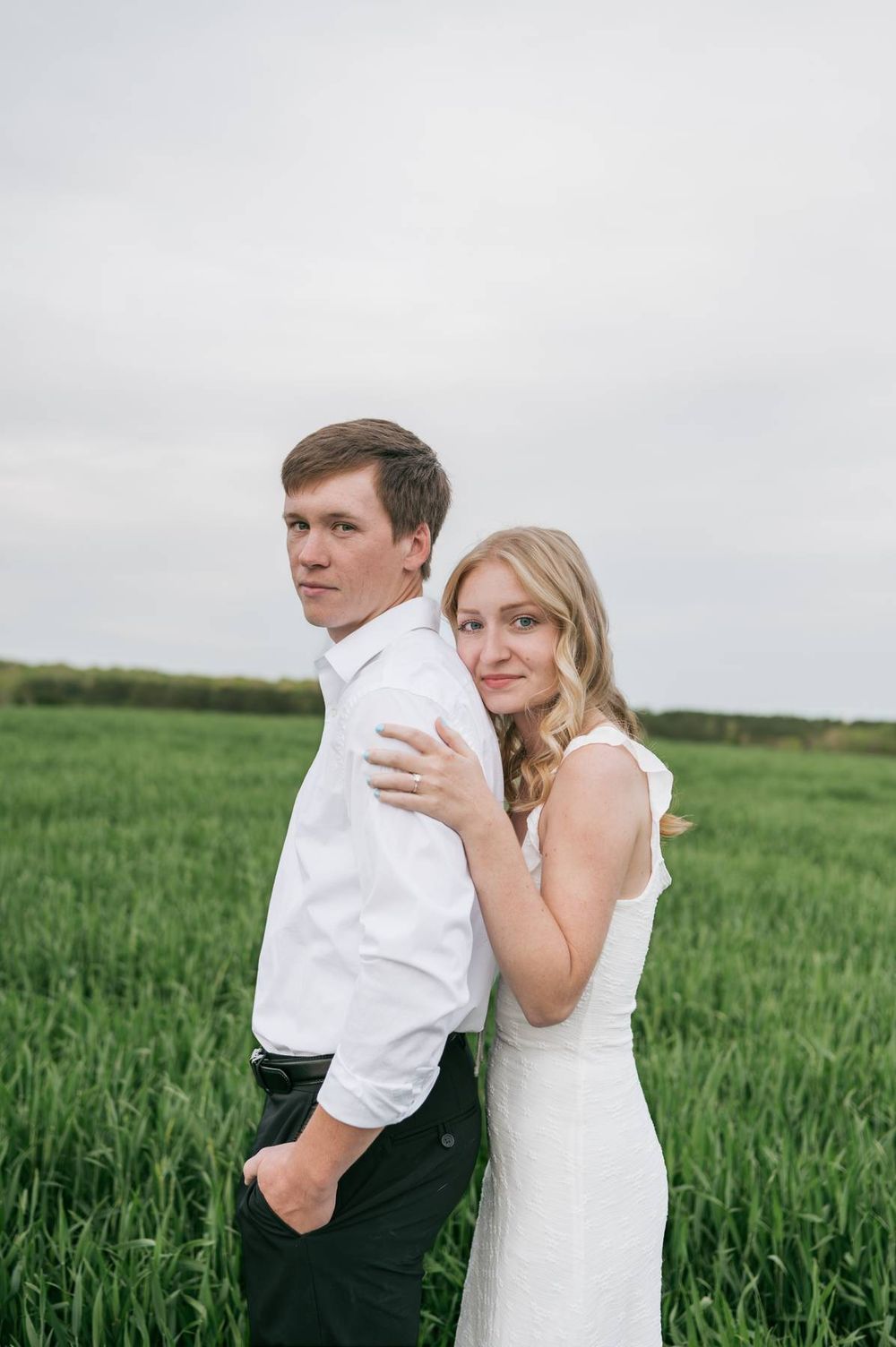Engaged couple posing back-to-back in a lush green field, woman in white dress smiling at camera, engagement photographer Asheboro NC