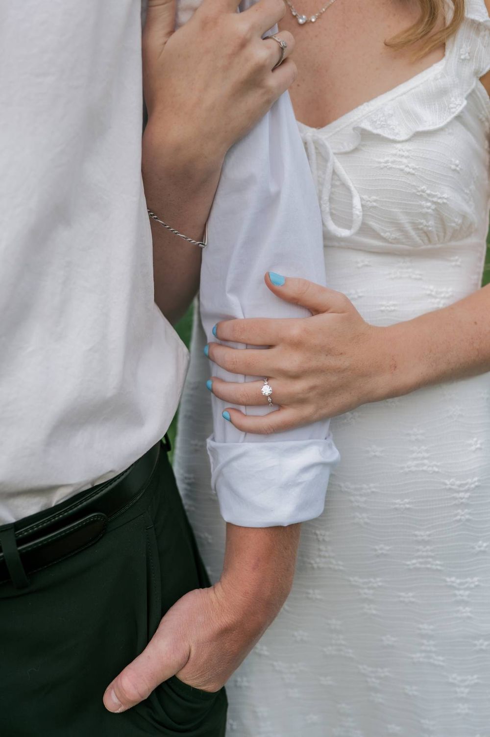 Close-up of bride and groom hands showing diamond engagement ring and bracelet in white attire, engagement photographer NC