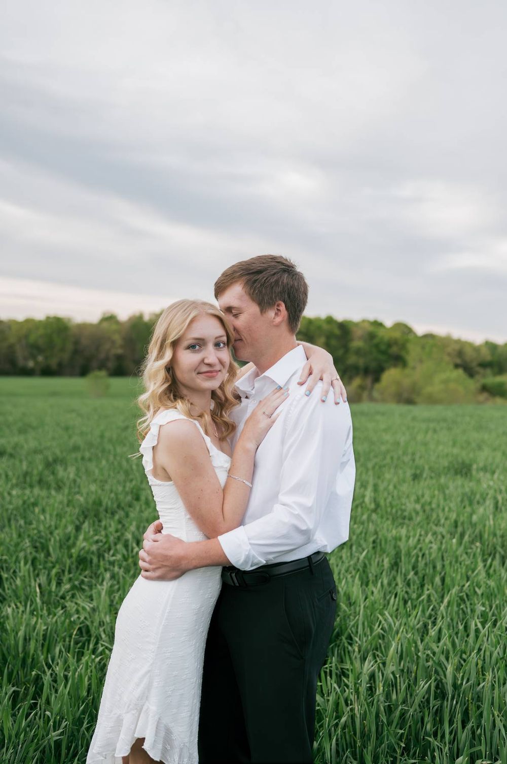 Romantic couple embracing in a green field at dusk, groom kissing bride's cheek during wedding photos, engagement photographer NC