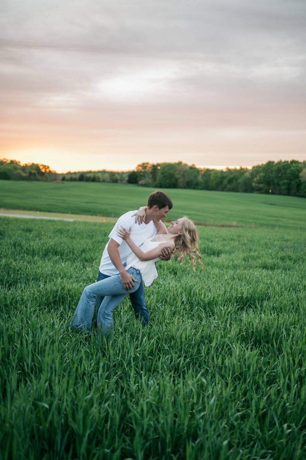 Couple sharing a romantic dip kiss in a lush green field at golden sunset, engagement photographer High Point NC