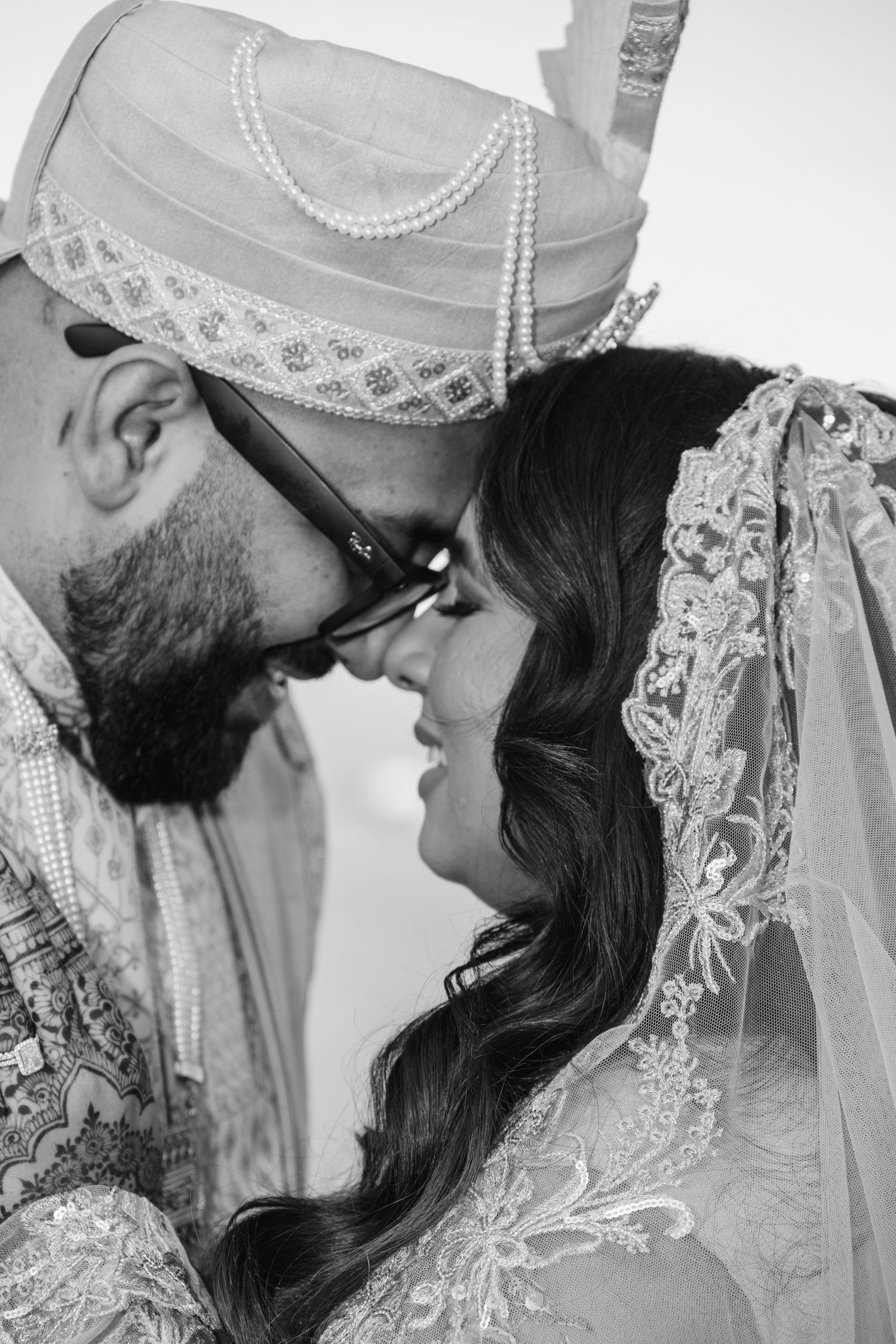 Black and white photo of South Asian bride and groom in traditional wedding attire sharing an intimate moment.