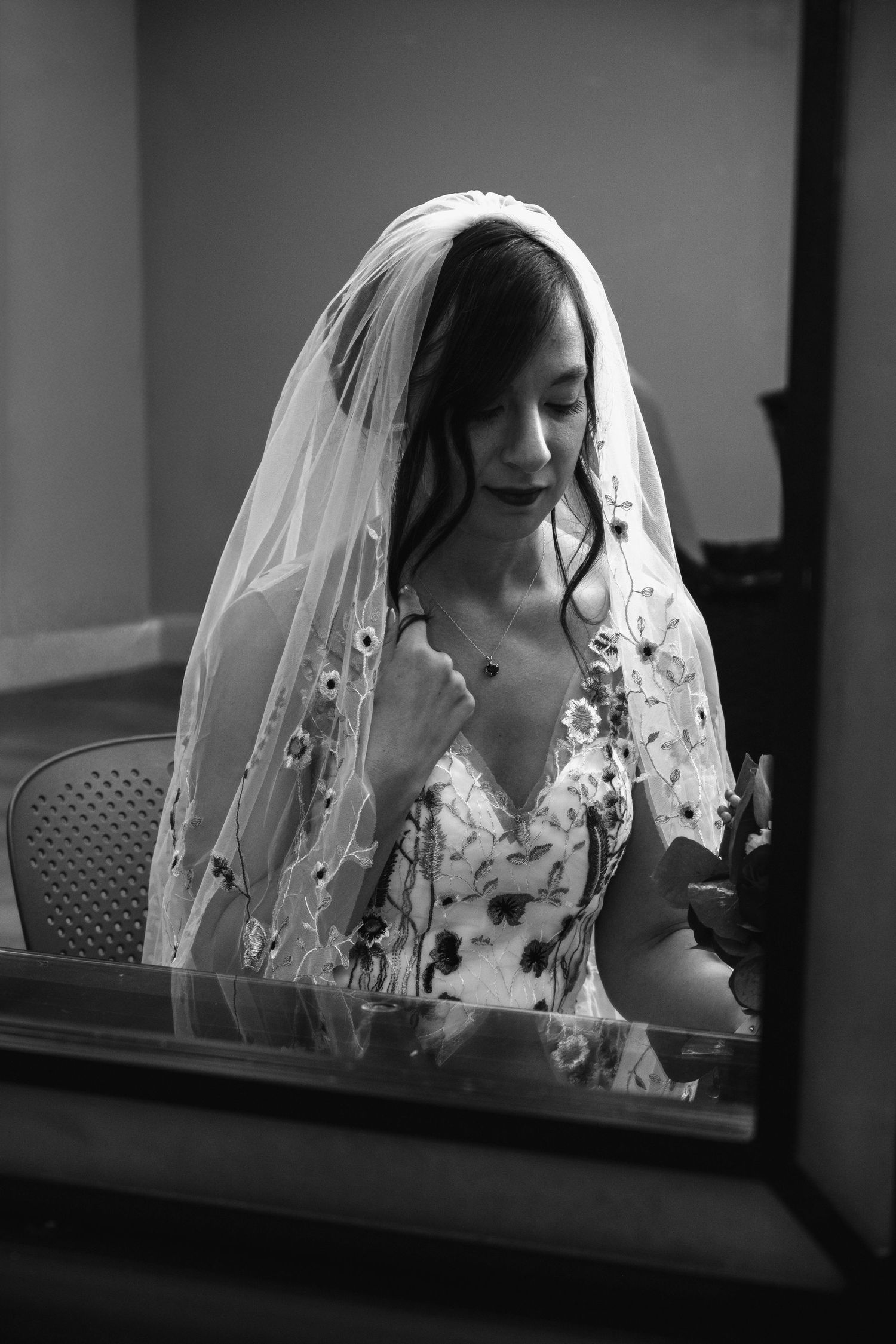 Black and white photo of a bride in a floral gown and veil, looking down gracefully before her wedding ceremony.