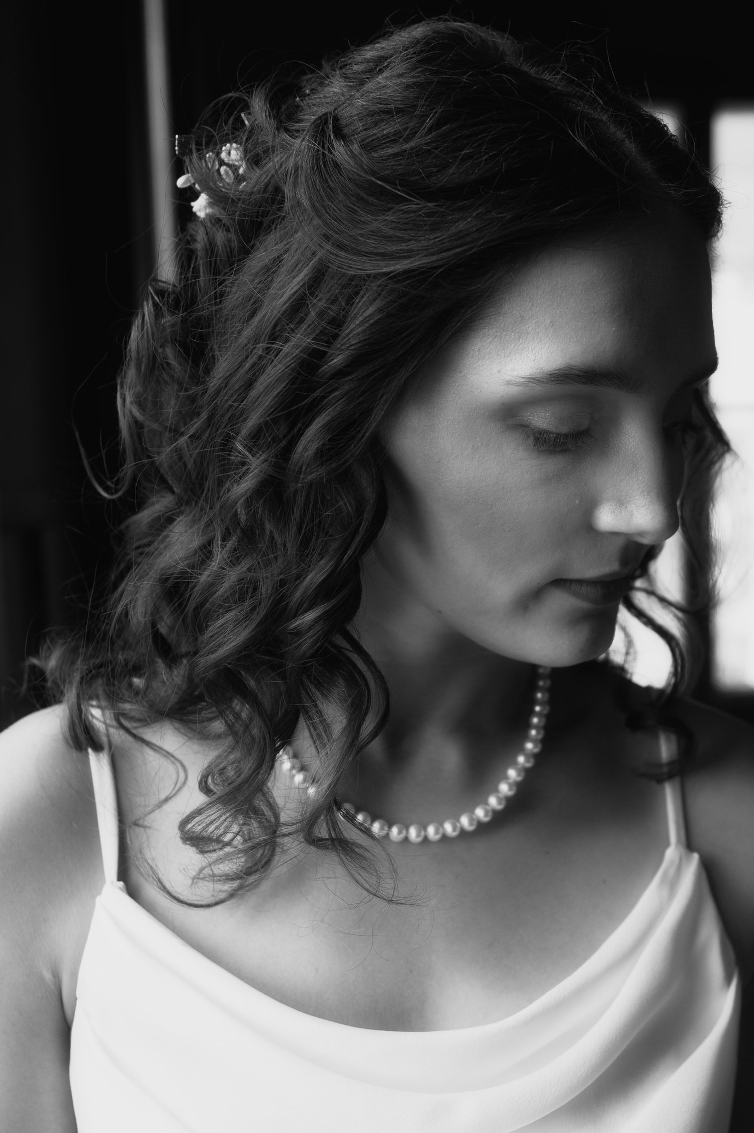 Black and white portrait of a bride with curly hair, pearl necklace, and floral hair accessory in a white dress.