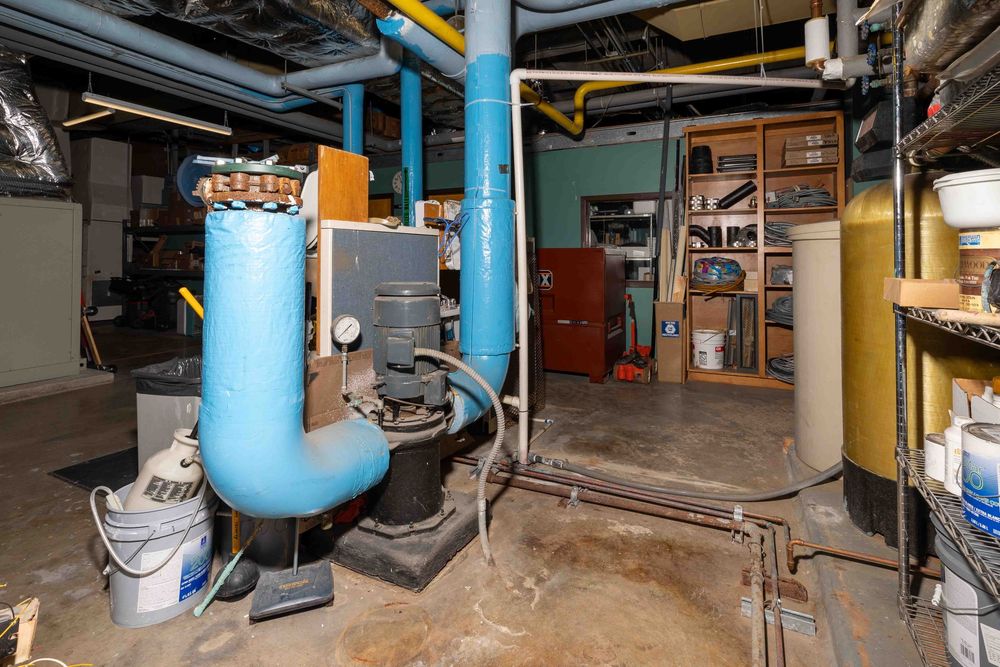 Basement utility room with blue pipes, boiler system, and mechanical equipment on concrete floor.