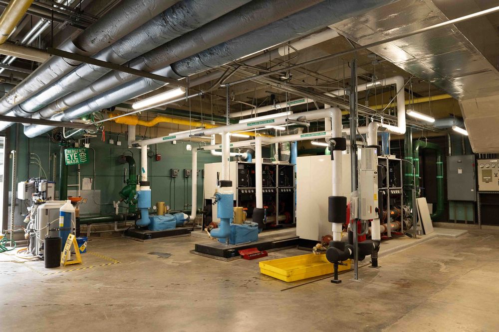 Industrial mechanical room with large HVAC equipment, pipes, and machinery in a commercial facility.