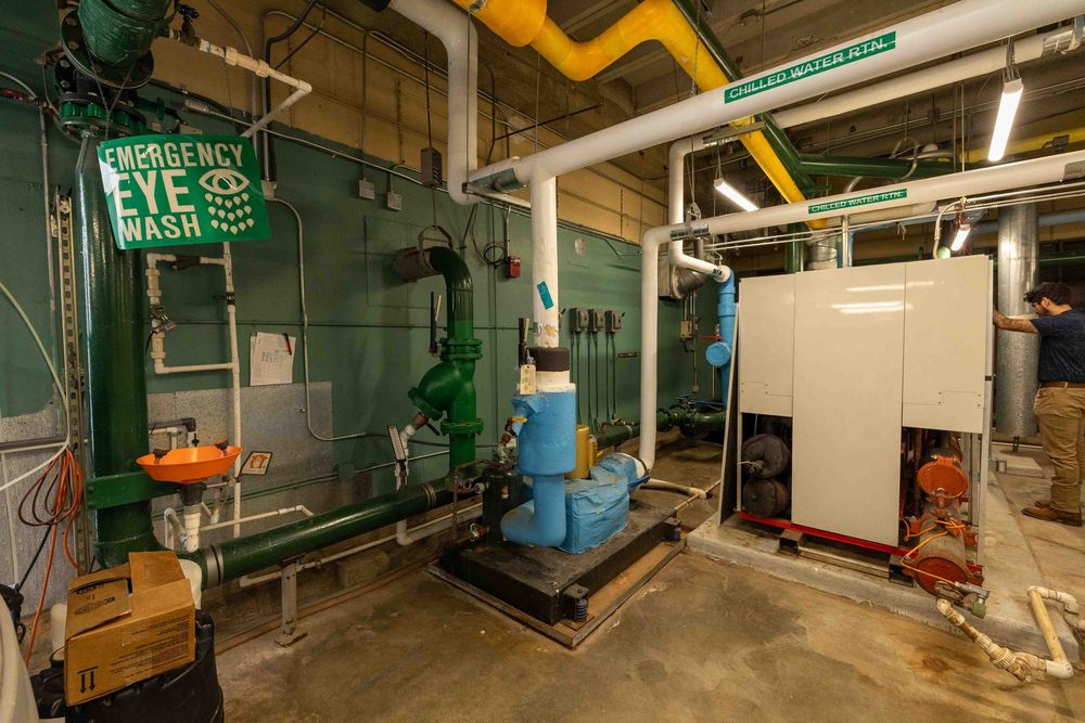 Industrial mechanical room with emergency eye wash station, pipes, pumps, and green equipment in a utility facility.