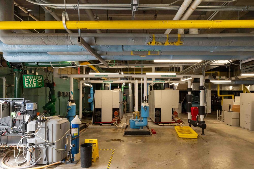 Industrial mechanical room with yellow pipes, HVAC equipment, and machinery on a concrete floor.