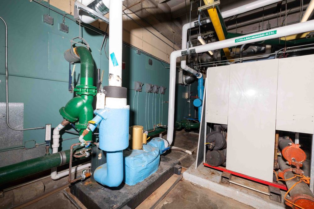 Industrial mechanical room with green pump, blue pipes, and white HVAC equipment in a commercial building.