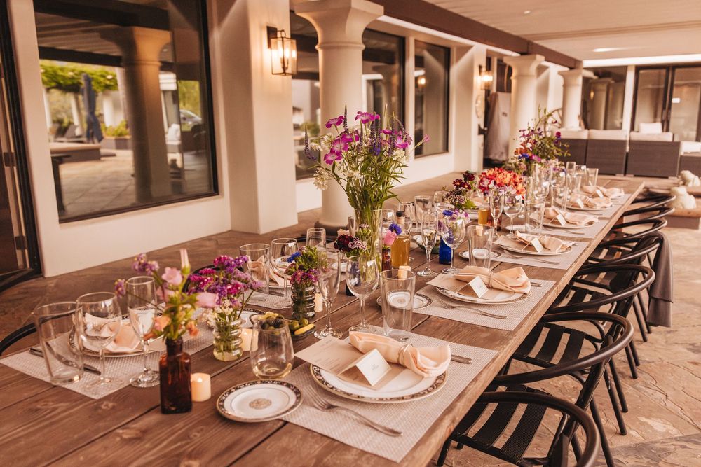 Elegant outdoor dining table set with floral centerpieces, glassware, and place settings for a formal event.