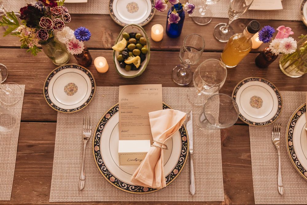 Elegant wedding table setting with floral centerpieces, gold-rimmed plates, crystal glasses, and peach napkins on a wooden table.