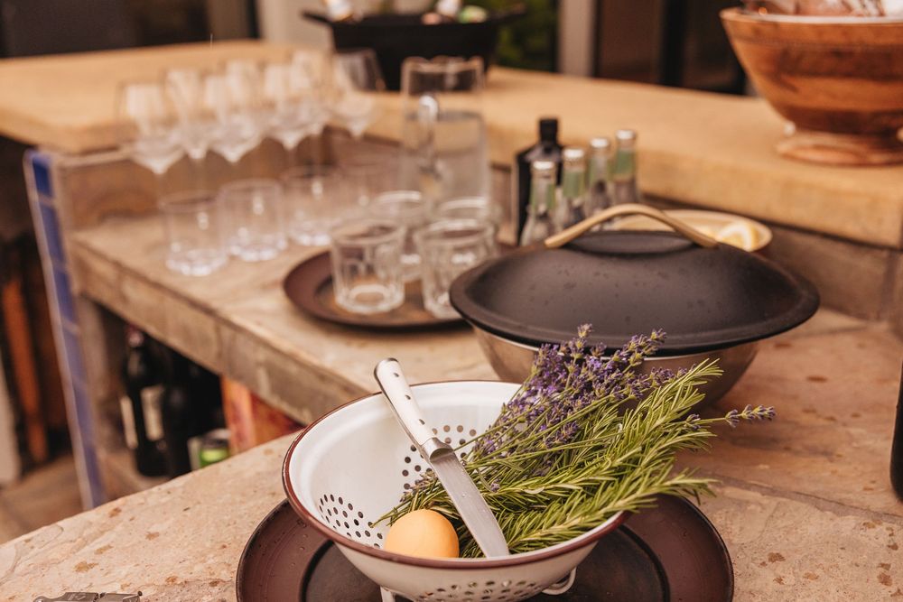 Rustic kitchen counter with a cast iron pot, herb bouquet, decorative bowl, and wine glasses in the background.